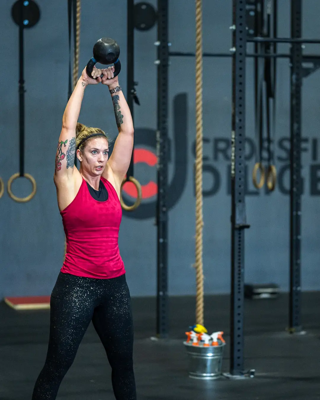 A member pressing a kettlebell overhead in front of the CrossFit Diligence logo